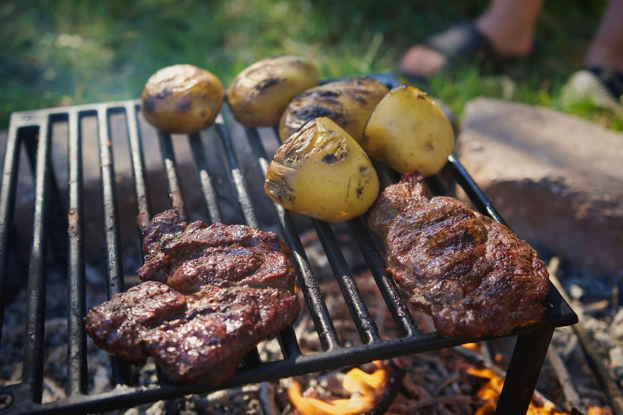 Steaks and potatoes cooking on a grate over a campfire